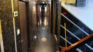 Un pasillo de hotel con piso de mármol, puertas y una escalera con barandilla de madera.
