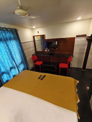 A hotel room with a bed, a desk with a chair, a television, and a window with curtains.
