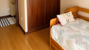 A bedroom with a wooden wardrobe, a bed with a leaf-patterned bedspread, and a white ceiling light. - Apartment '2 Bedroom  On The Beach' with Sea View and Wi-Fi (Moaña)