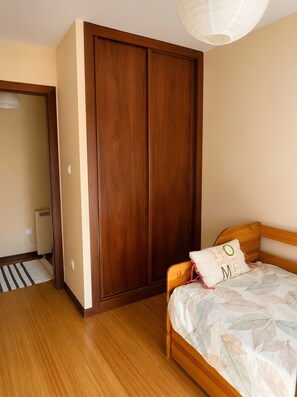 Ein Schlafzimmer mit einem Holzschrank, einem Bett mit blattgemustertem Überwurf und einer weißen Deckenleuchte.