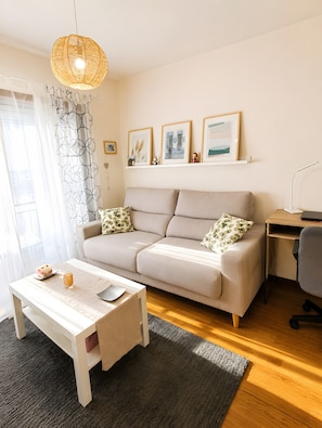 A modern living room with a sofa, a coffee table, a desk, and a lamp. There are framed pictures on the wall and a window with curtains. - Apartment '2 Bedroom  On The Beach' with Sea View and Wi-Fi (Moaña)