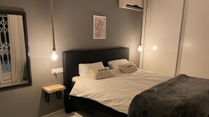 Een moderne slaapkamer met een zwart hoofdbord, een nachtkastje, een hanglamp en een ingelijst schilderij aan de muur.