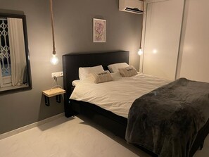 Ein modernes Schlafzimmer mit einem schwarzen Kopfteil, einem Nachttisch, einer Hängeleuchte und einem gerahmten Bild an der Wand.