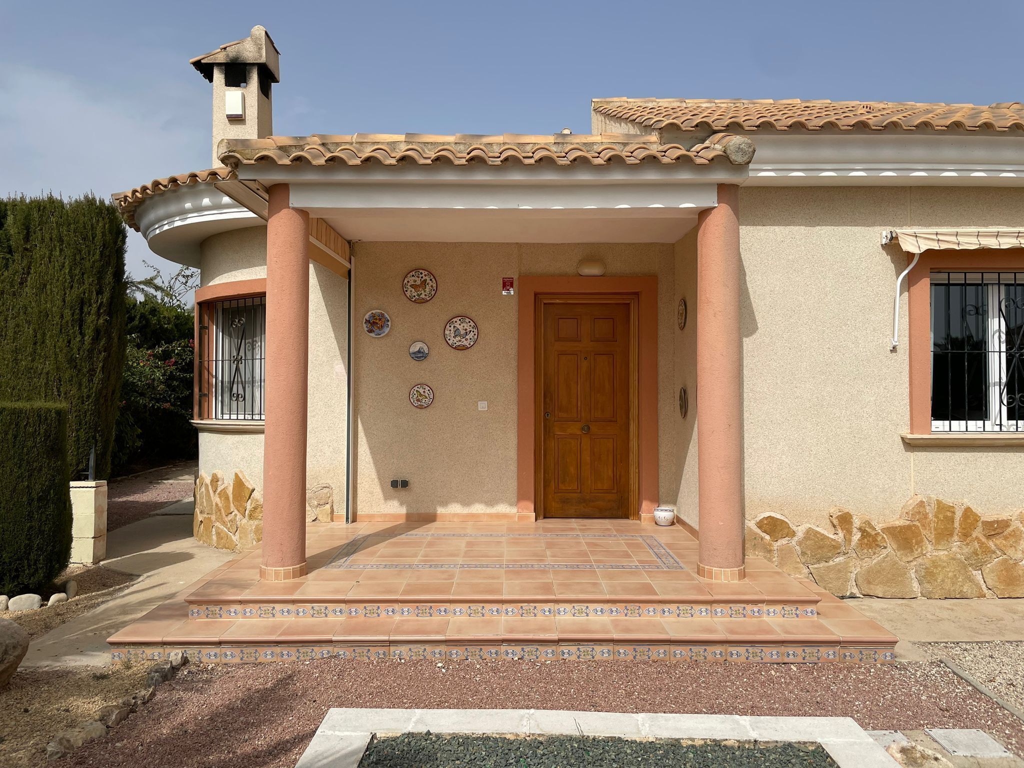 A house with a tiled entrance, a wooden door, and decorative plates on the wall.