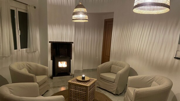 Een gezellige woonkamer met een open haard, twee fauteuils, een salontafel en twee hanglampen.