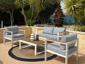 An outdoor seating area with white furniture, a woven rug, and tropical plants. - Beautiful villa with a pool, ideal for 1 or 2 families (Busot)