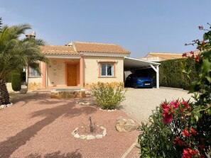Uma casa com telhado de telhas, garagem e entrada com um círculo de pedras e plantas.