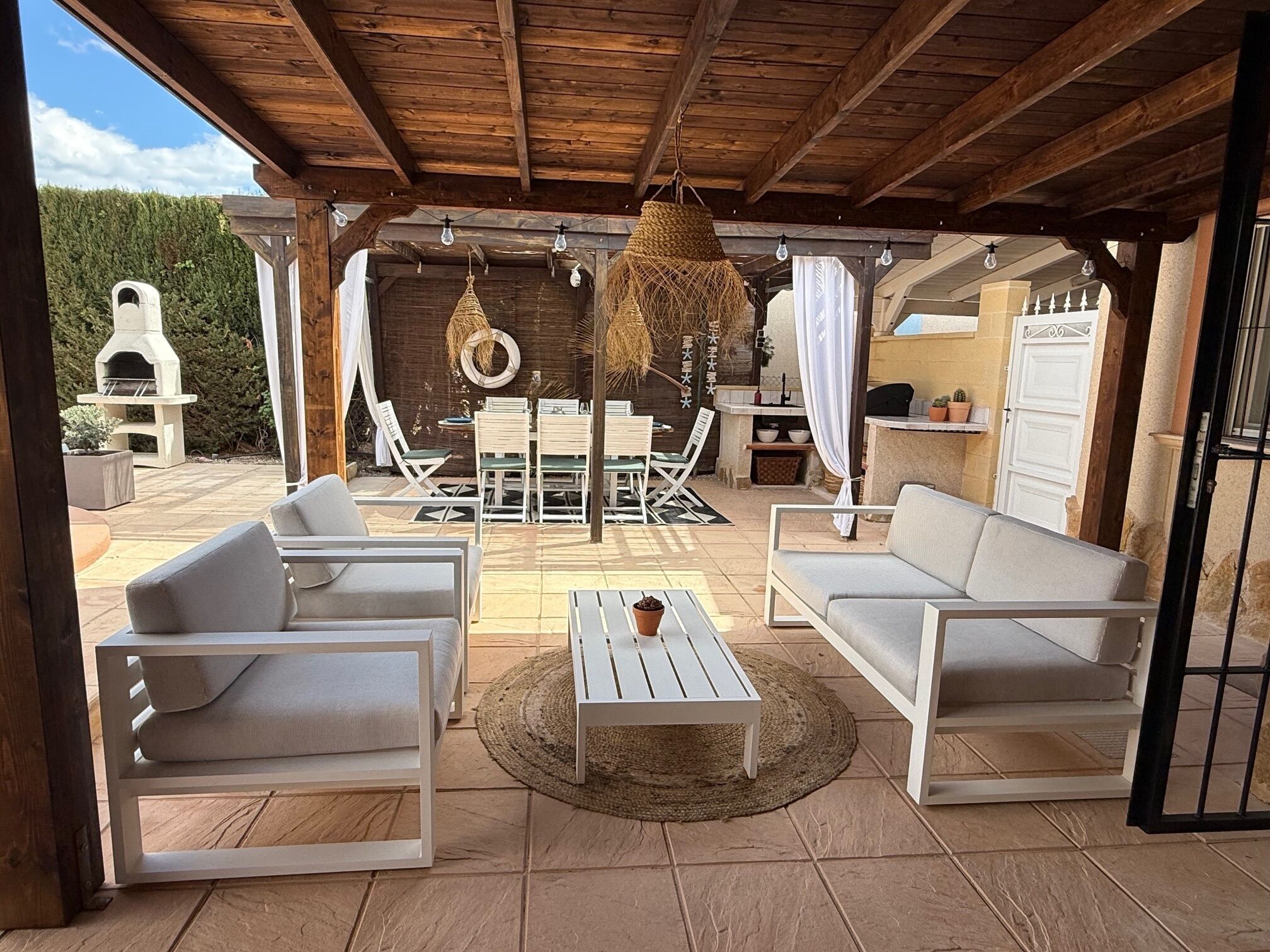 An outdoor patio with white furniture, a hanging light fixture, and a stone fireplace.