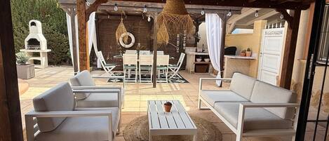 An outdoor patio with white furniture, a hanging light fixture, and a stone fireplace.