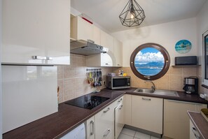 A compact kitchen with a built-in microwave, a sink, and a window with a view of the sea. - Ti Bato: Apartment with ocean views and the beach within walking distance (Les Trois-Ilets)
