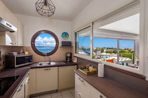 A modern kitchen with a round window, a built-in microwave, and a view of the sea. - Ti Bato: Apartment with ocean views and the beach within walking distance (Les Trois-Ilets)