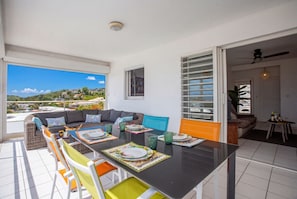 A dining area with a table set for four, a sofa, and a view of the landscape. - Ti Bato: Apartment with ocean views and the beach within walking distance (Les Trois-Ilets)