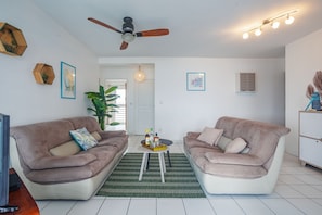 Ein Wohnzimmer mit zwei Sofas, einem Deckenventilator, einem Couchtisch und einer großen Pflanze.