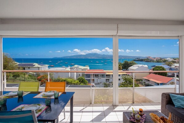 A balcony with a view of the sea and boats, a table with plates and glasses, and a wicker sofa. - Ti Bato: Apartment with ocean views and the beach within walking distance (Les Trois-Ilets)