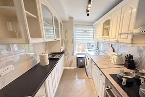 A kitchen with white cabinets, a black countertop, and a window with blinds. - Mayfair Beautiful Family Apartment (London)