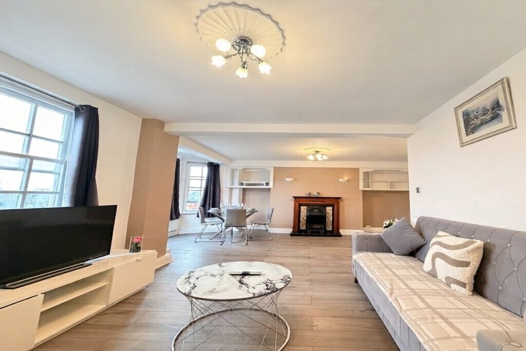 A modern living room with a flat-screen TV, a marble coffee table, a sofa, and a fireplace.