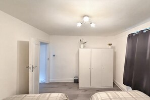 A bedroom with a wardrobe, a door leading to another room, and a bed with a patterned bedspread. - Mayfair Beautiful Family Apartment (London)