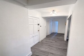 A hallway with white walls and wooden flooring, leading to a door at the end. - Mayfair Beautiful Family Apartment (London)