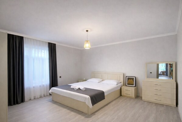 A bedroom with a bed, bedside tables, a dresser, a mirror, and a hanging light fixture.