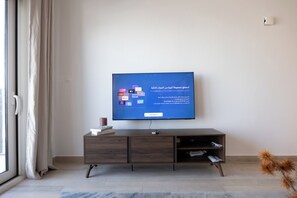 Ein modernes Wohnzimmer mit einem flachbildfernseher, der an einem Holzschrank befestigt ist, einem Fenster mit Vorhängen und einer kleinen Pflanze auf dem Boden.
