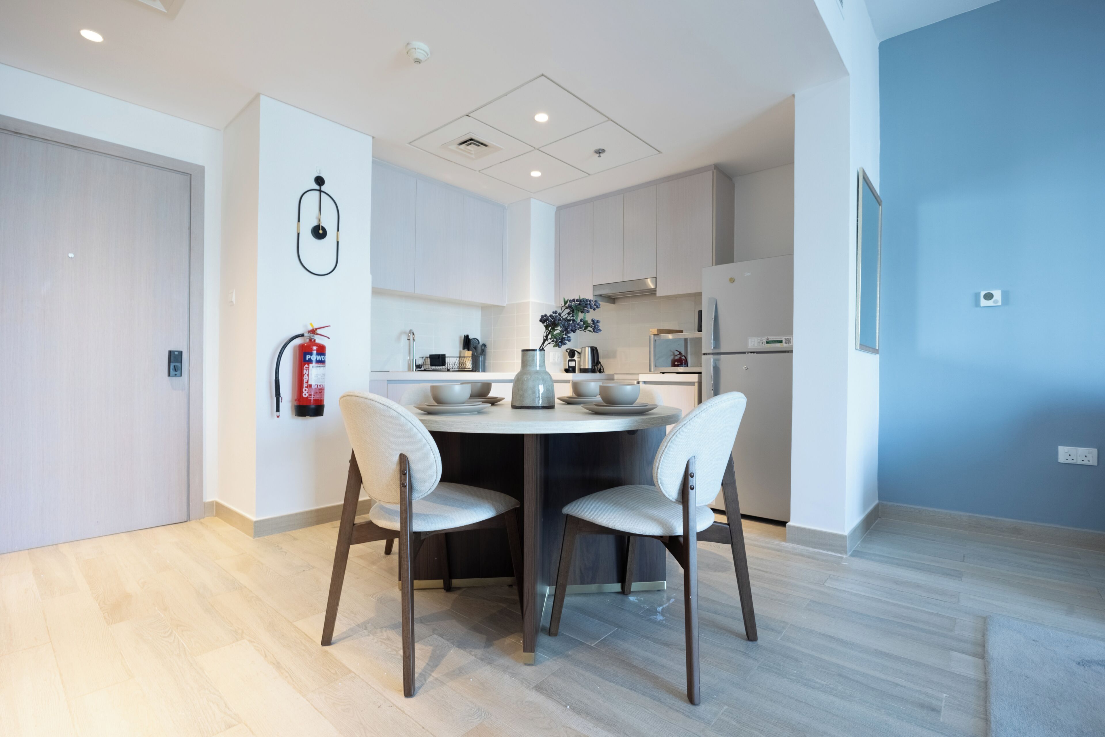 Une cuisine moderne dotée d’un îlot central, de meubles blancs et d’un extincteur fixé au mur.