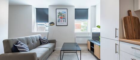 A modern living room with a sofa, a glass coffee table, and a kitchen area with cabinets and a countertop.
