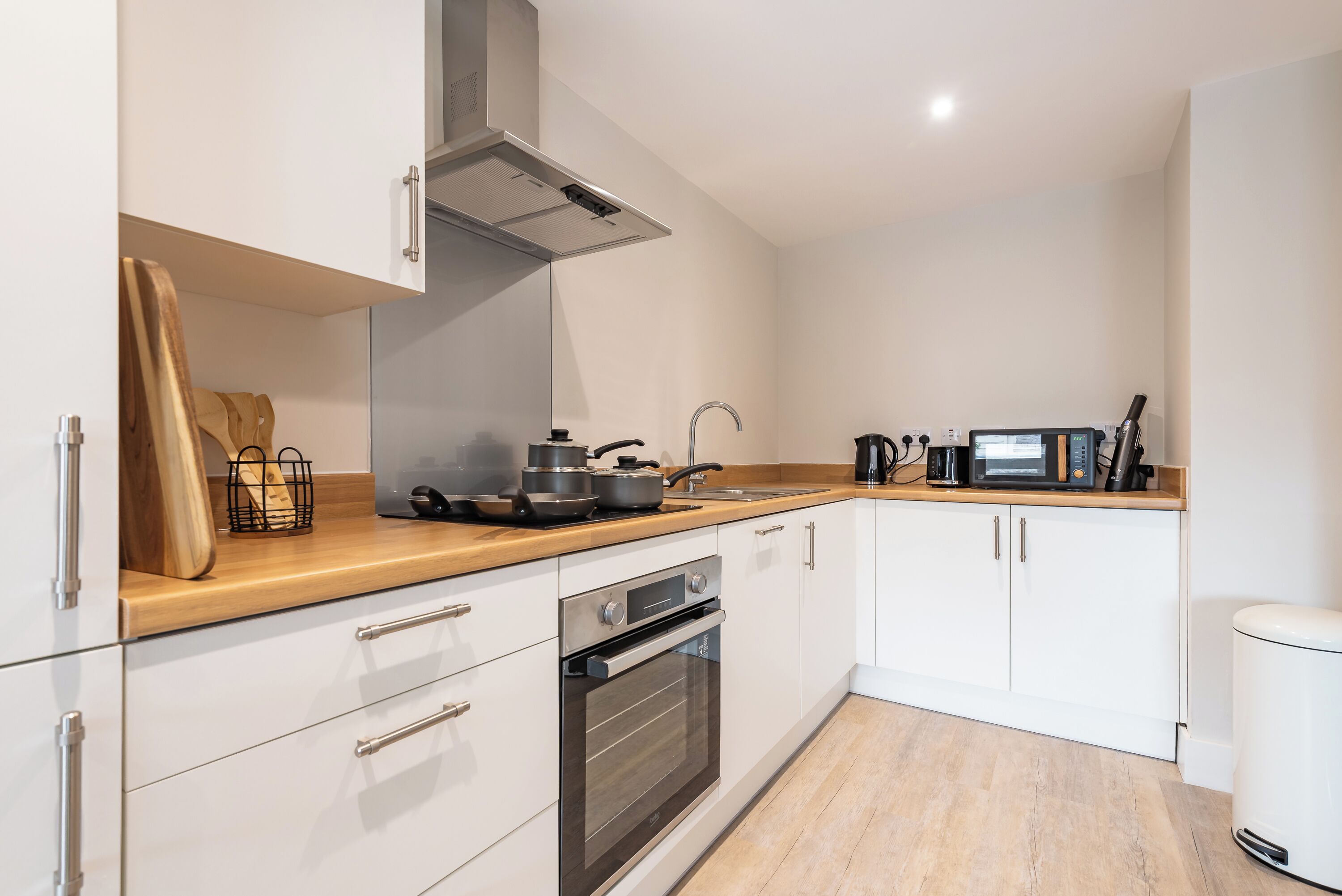 A modern kitchen with white cabinetry, a wooden countertop, an oven, a microwave, and a stainless steel range hood.