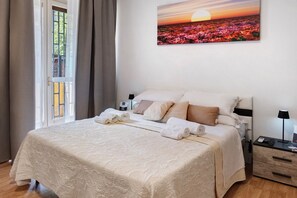 A neatly made bed with a patterned bedspread, a bedside table with a lamp, and a painting of flowers on the wall. - Home Joséphine - Caserta - Triple Room with Private Bathroom (Caserta)