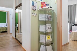 A hotel room with a glass partition, a bed with a green bedspread, a coffee bar, and various informational signs. - Home Joséphine - Caserta - Triple Room with Private Bathroom (Caserta)
