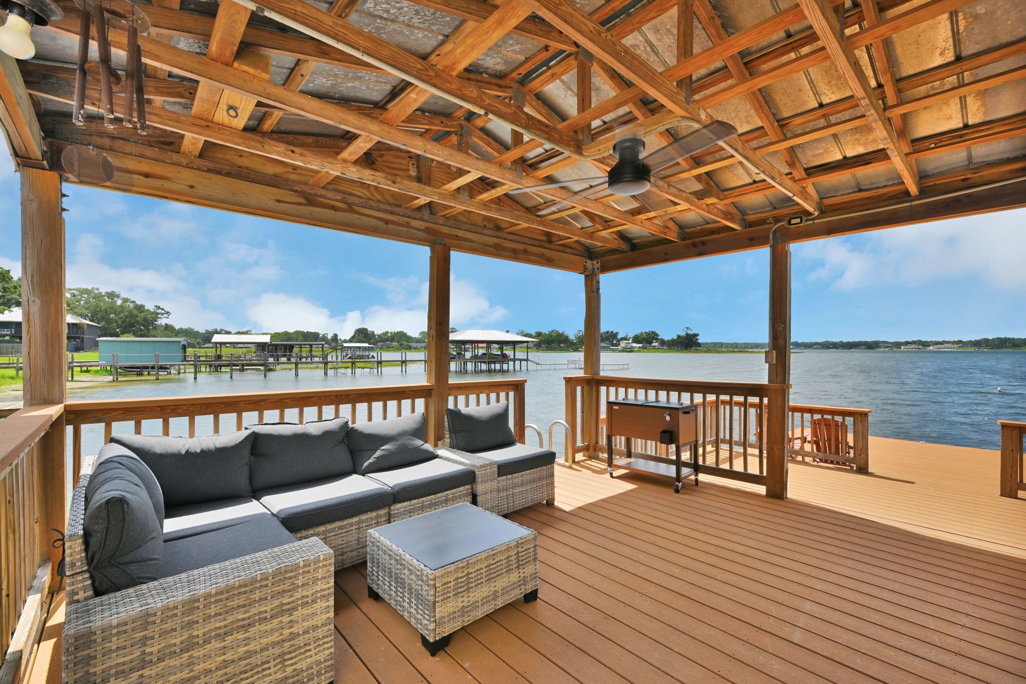 A covered outdoor deck with a wooden floor, a sofa set, and a view of a body of water.