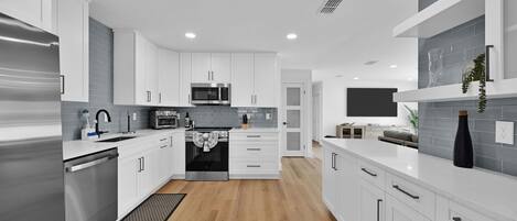 A modern kitchen with white cabinetry, stainless steel appliances, and a wooden floor.