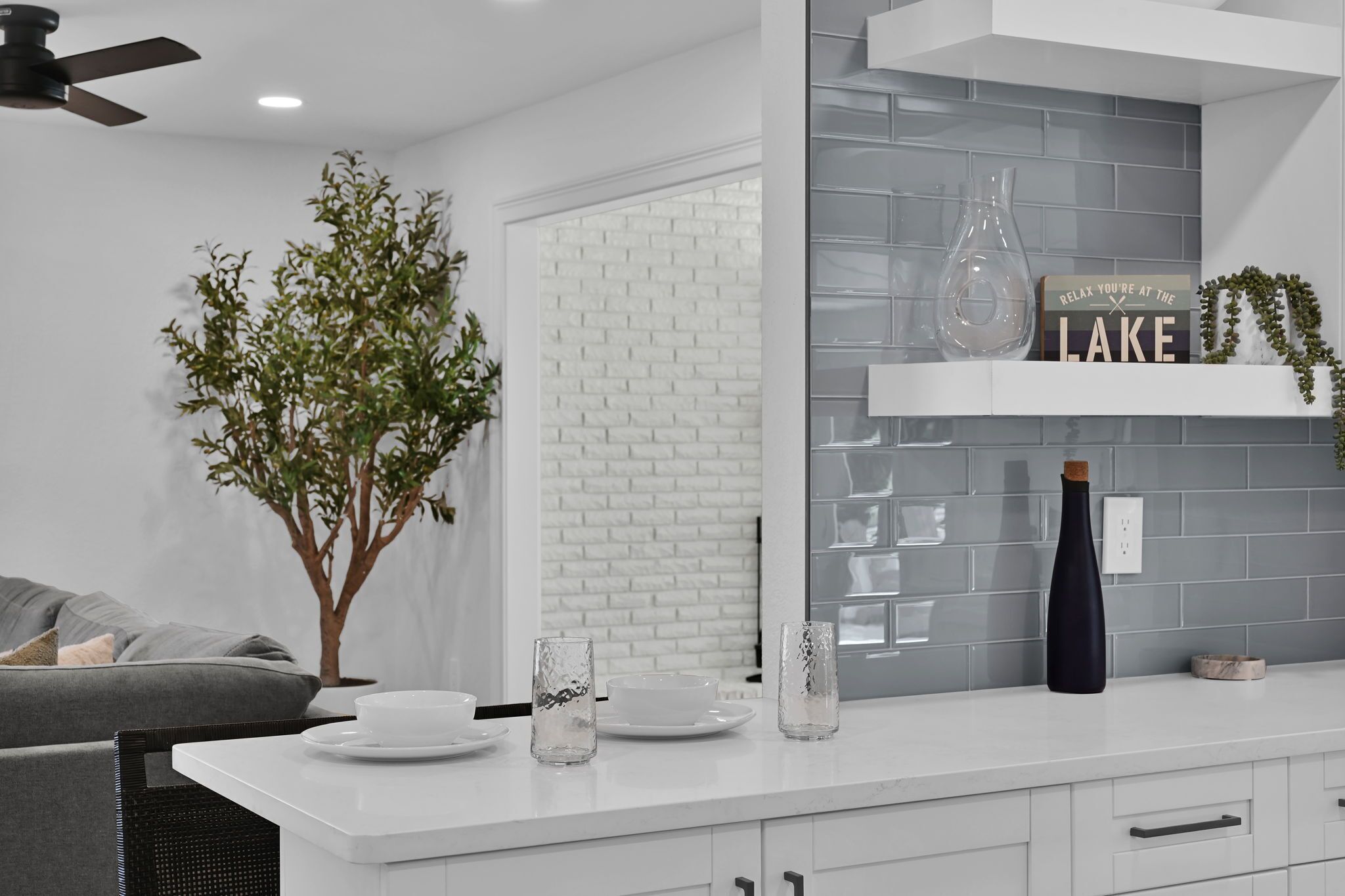 A modern kitchen with white cabinetry, a brick backsplash, and a decorative shelf with a sign.