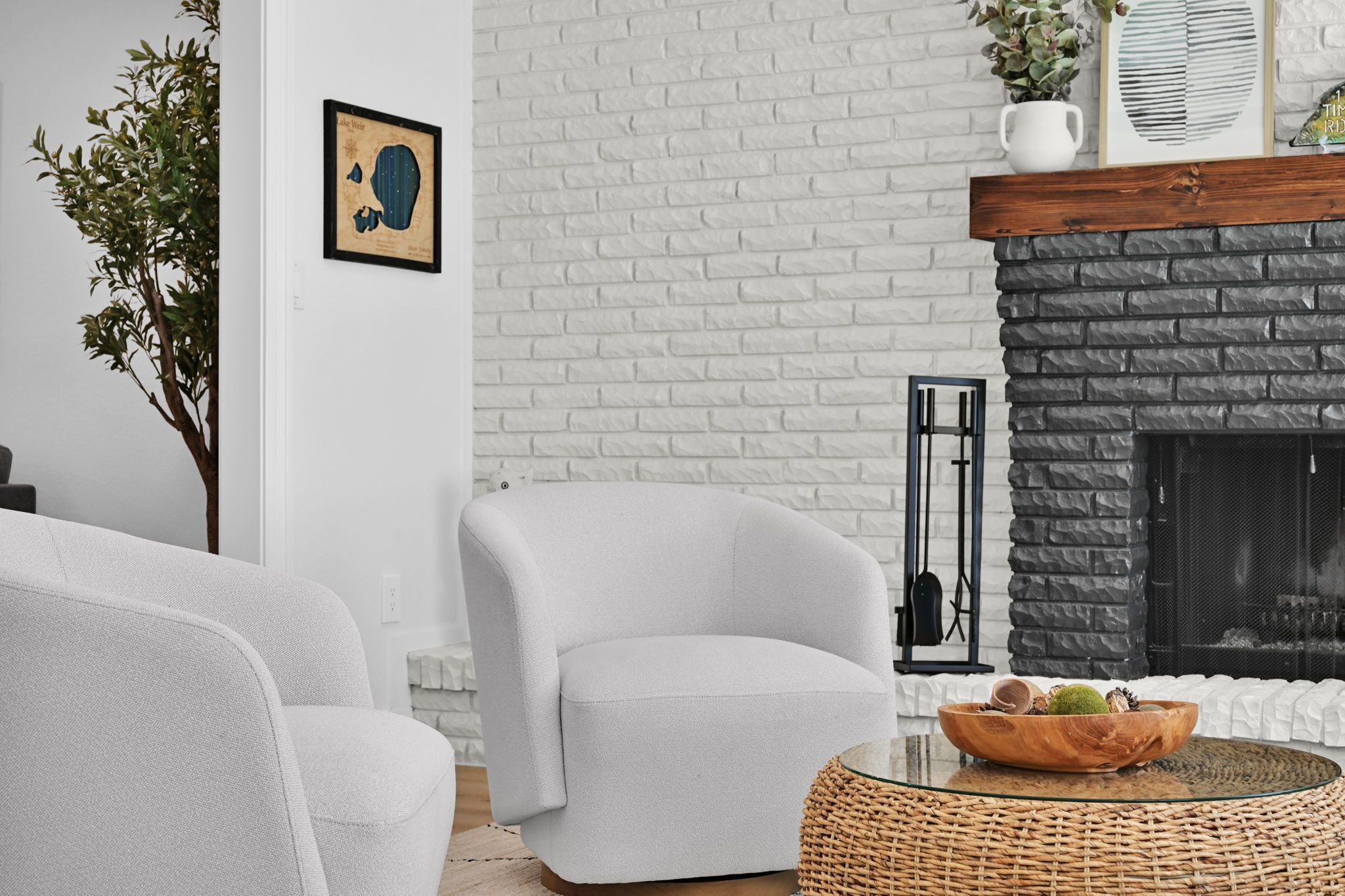 Una sala de estar moderna con una chimenea de ladrillo blanco, un sillón blanco y una mesa de centro de mimbre con un cuenco de frutas.