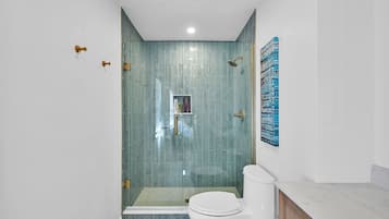 A modern bathroom with a glass-enclosed shower, a toilet, and a marble countertop.