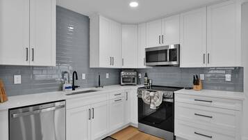 A modern kitchen with white cabinets, a stainless steel dishwasher, a built-in oven, a microwave, and a black countertop.