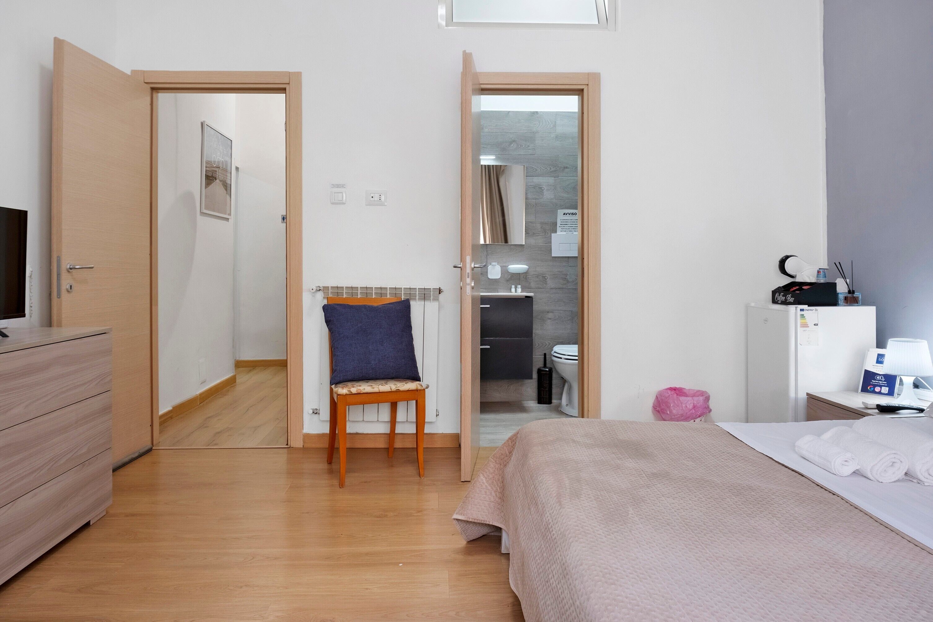 A hotel room with a bed, a chair, a dresser, a desk with a lamp, and a bathroom visible through an open door.