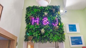 A wall with a neon sign spelling 'H&J' and a framed award certificate for 'Home Joséphine - CASERTA' on a green wall. - Home Joséphine - Caserta - Quadruple Room with Private Bathroom (Caserta)