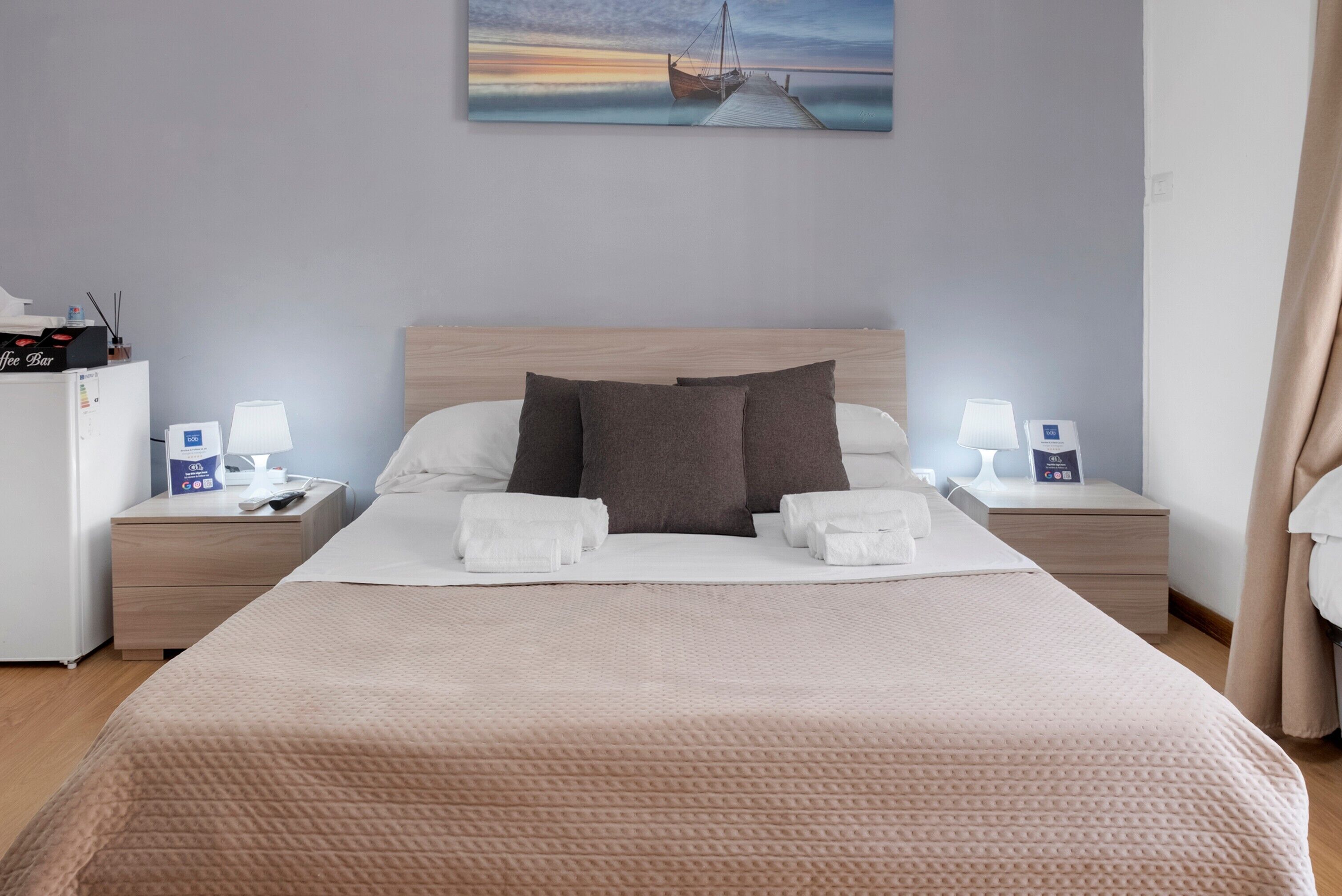 Une chambre d’hôtel avec un lit, deux tables de chevet, un coin café et un tableau au mur.