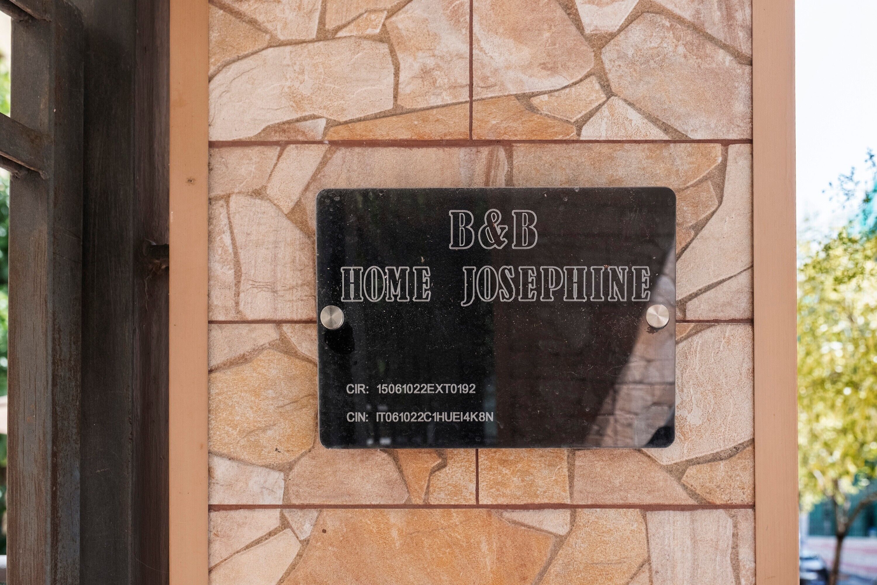 A black metal plaque with 'B&B HOME JOSEPHINE' and two identification numbers on a stone wall.