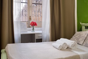 Quarto de hotel com cama, escrivaninha, um vaso com flores e parede verde.