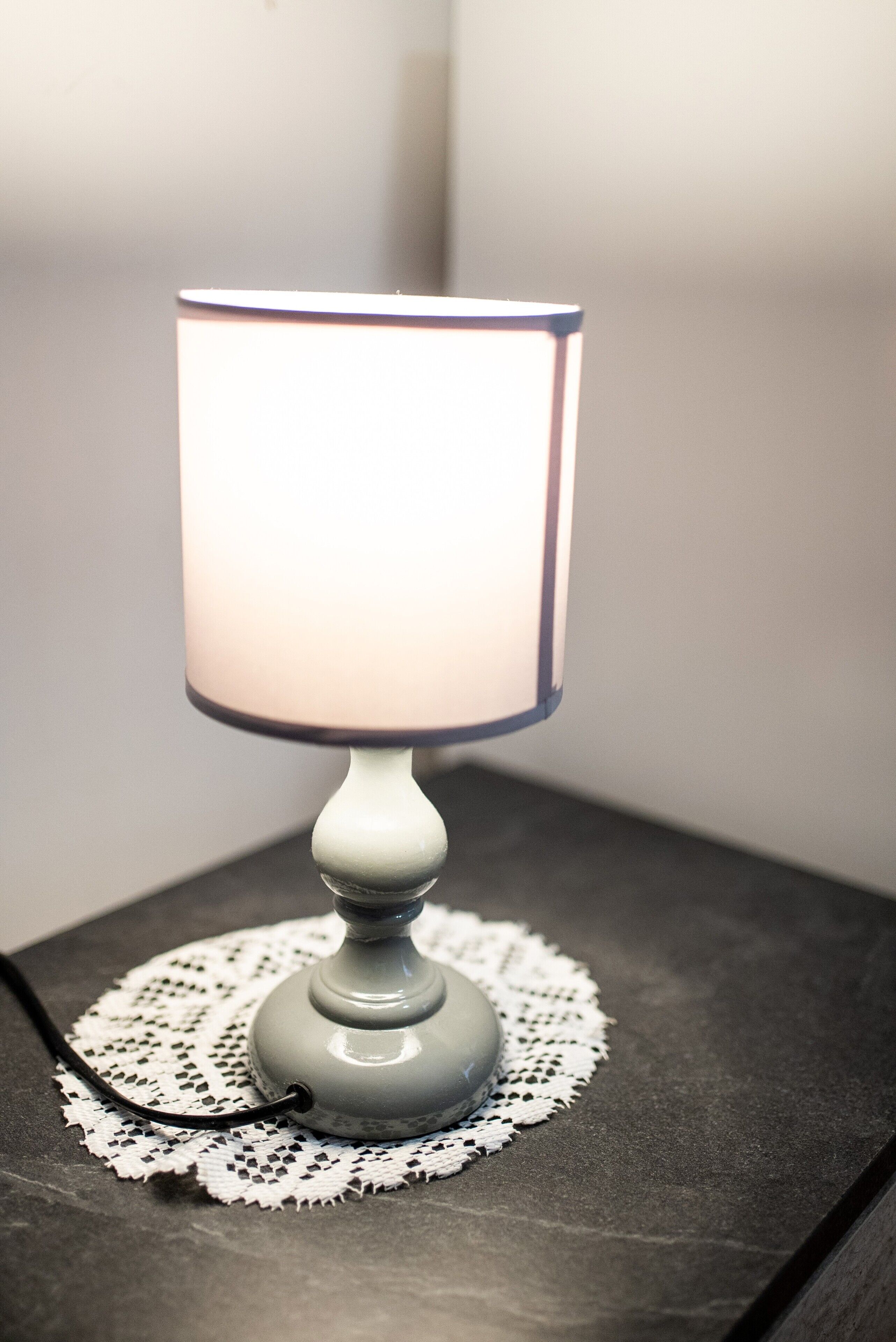 A table lamp with a white shade and a blue rim, placed on a doily-covered table.