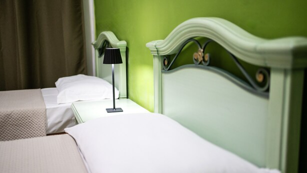 Ein Hotelzimmer mit zwei Betten, jedes mit einer weißen Matratze und einer schwarzen Lampe.