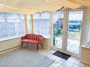Ein Zimmer mit einem roten Sofa, einem gemusterten Teppich und Blick auf einen Garten durch eine Glastür.