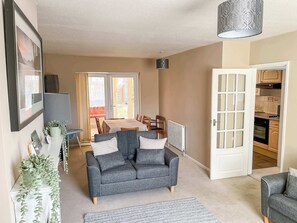 Ein Wohnzimmer mit grauem Sofa, einem Esstisch und einem durchgegangenen Durchgang zur sichtbaren Küche.