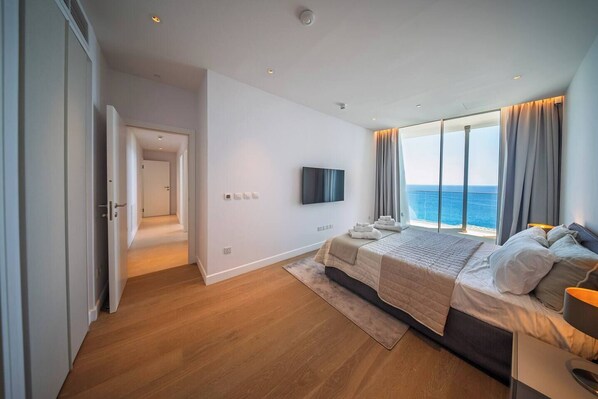 Ein modernes Schlafzimmer mit einem großen Bett, einem Flachbildfernseher und Meerblick.