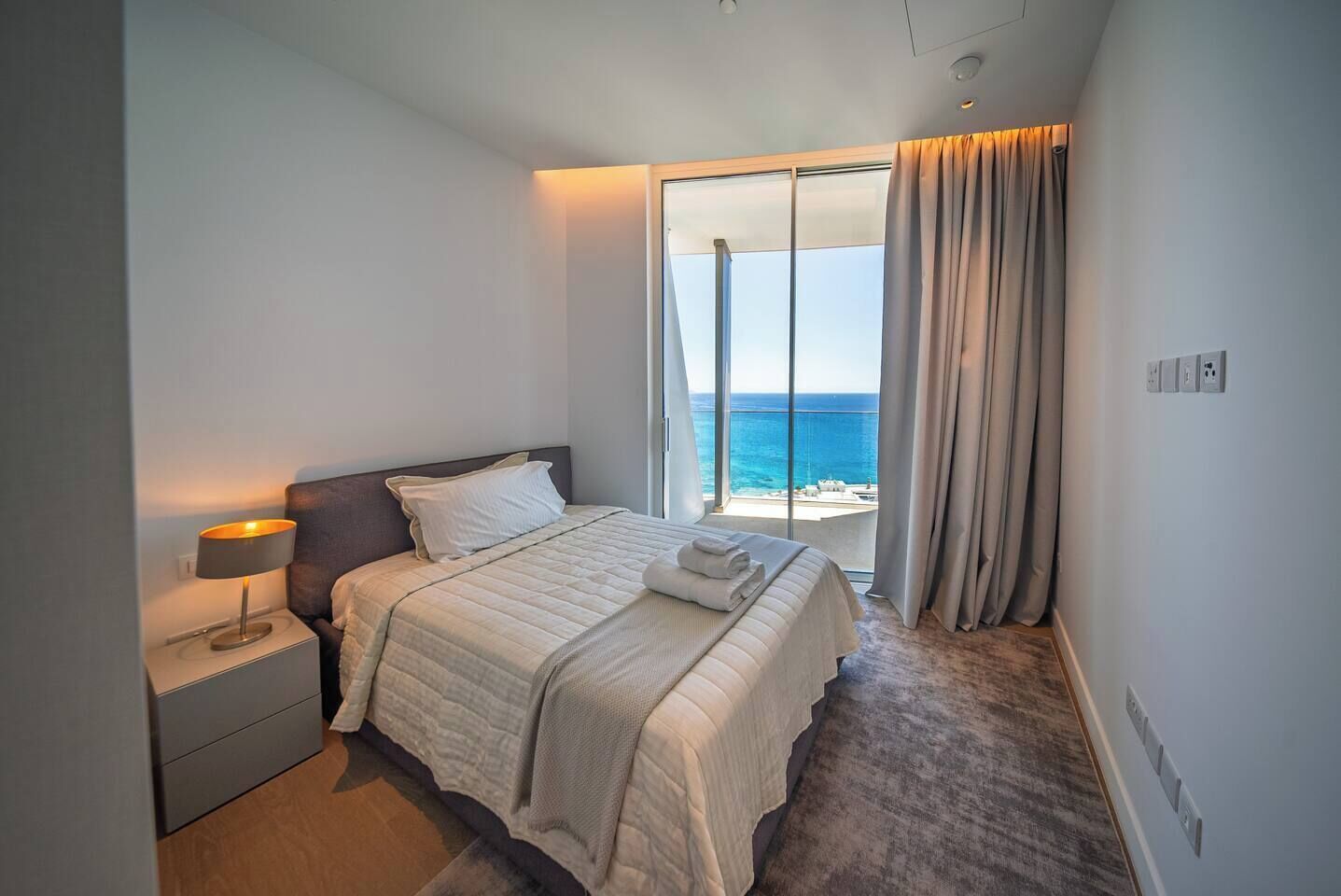 Een slaapkamer met een bed, nachtkastje en uitzicht op zee.