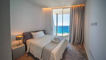 Een slaapkamer met een bed, nachtkastje en uitzicht op zee.