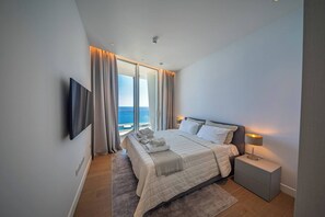 A modern bedroom with a large bed, a flat-screen TV, and a view of the sea. - Napa Horizon | Sea Front | Marina Tower 1702 (Ayia Napa)