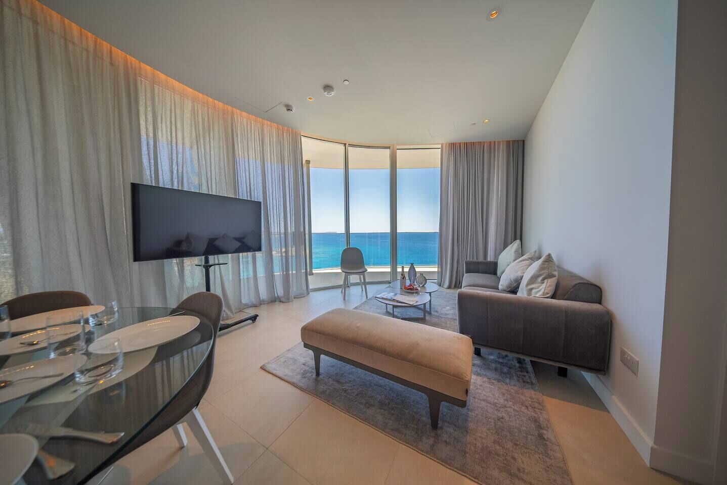 Een moderne woonkamer met een flatscreen televisie, een eettafel gedekt voor twee personen, een bank en een salontafel.