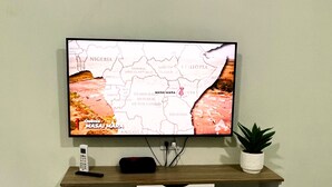Un televisor montado en la pared con un mapa mostrado, un control remoto y una pequeña planta en un estante debajo.